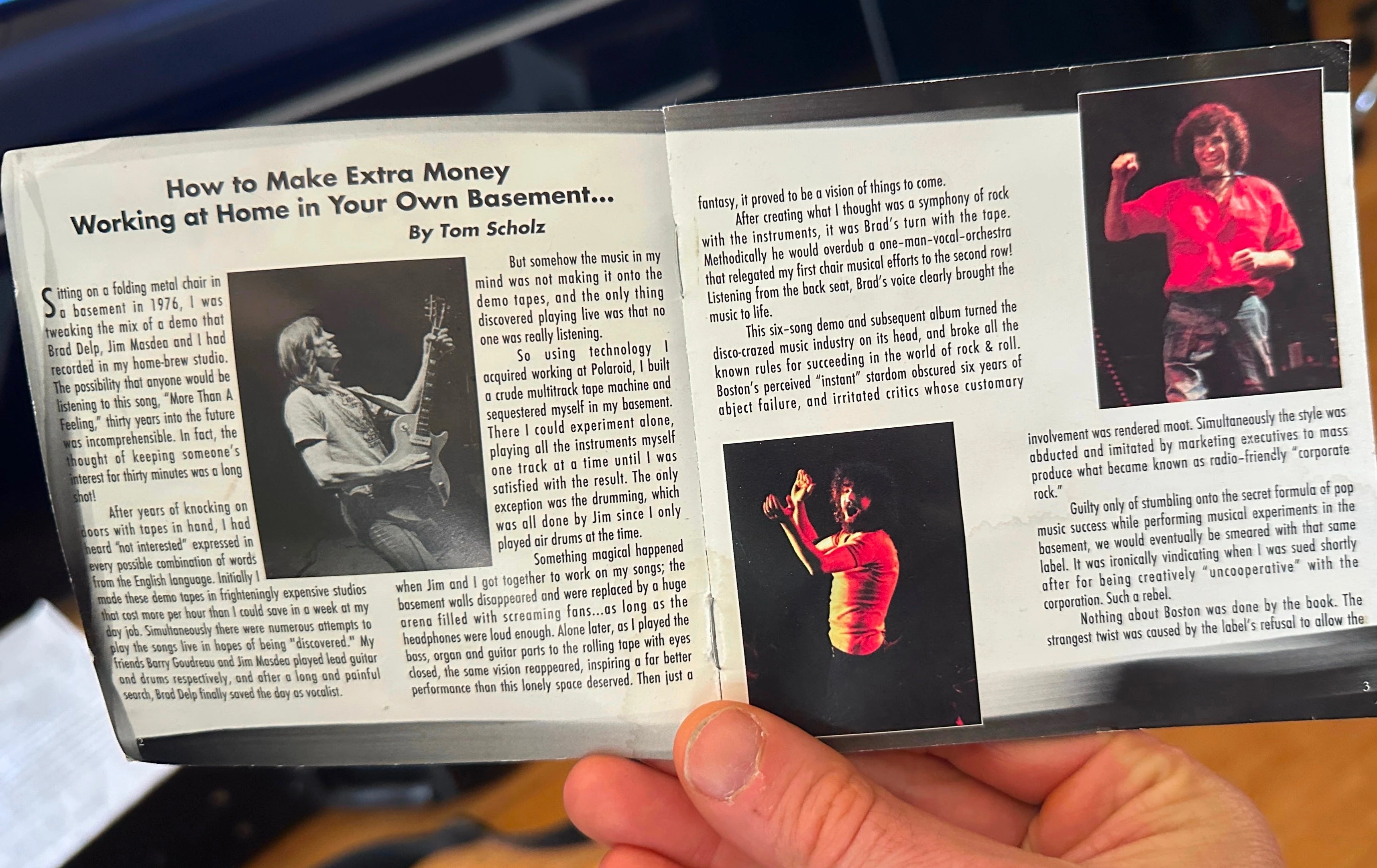 A hand holding an open booklet showing a Tom Scholz essay with concert photographs.