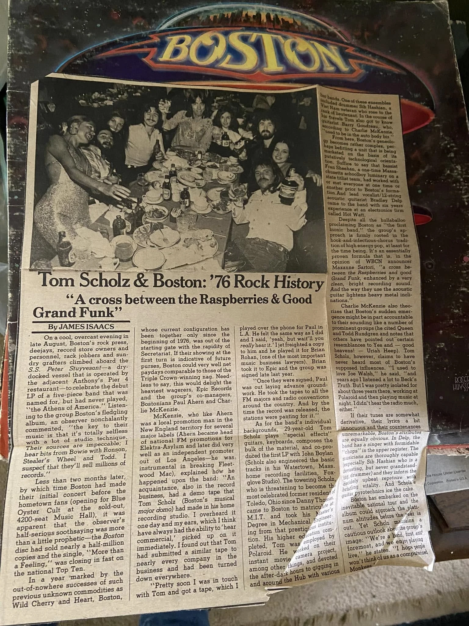 Torn newspaper clipping about Boston resting on the band's debut album cover, with a photo of a celebratory dinner party.